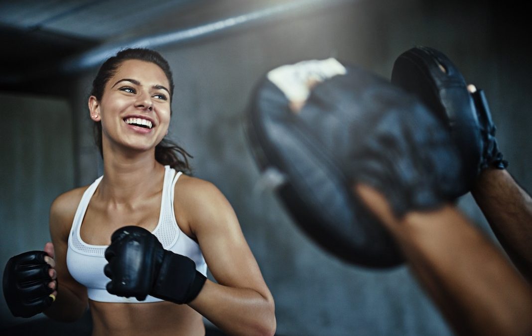 A woman smiles as she enjoys a boxing session with her trainer
